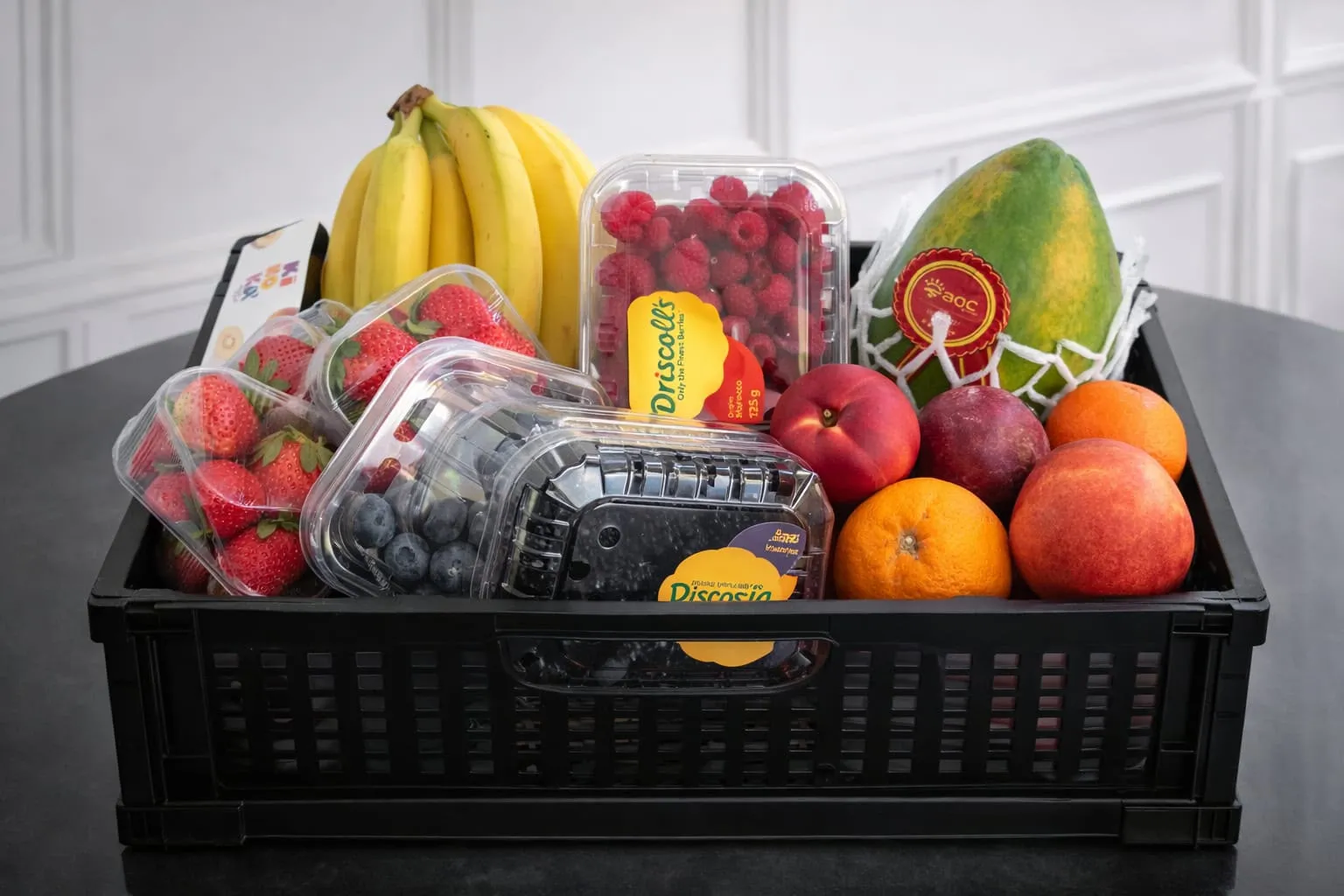 Zwarte krat vol aardbeien, frambozen, bessen, bananen, papaya en citrus