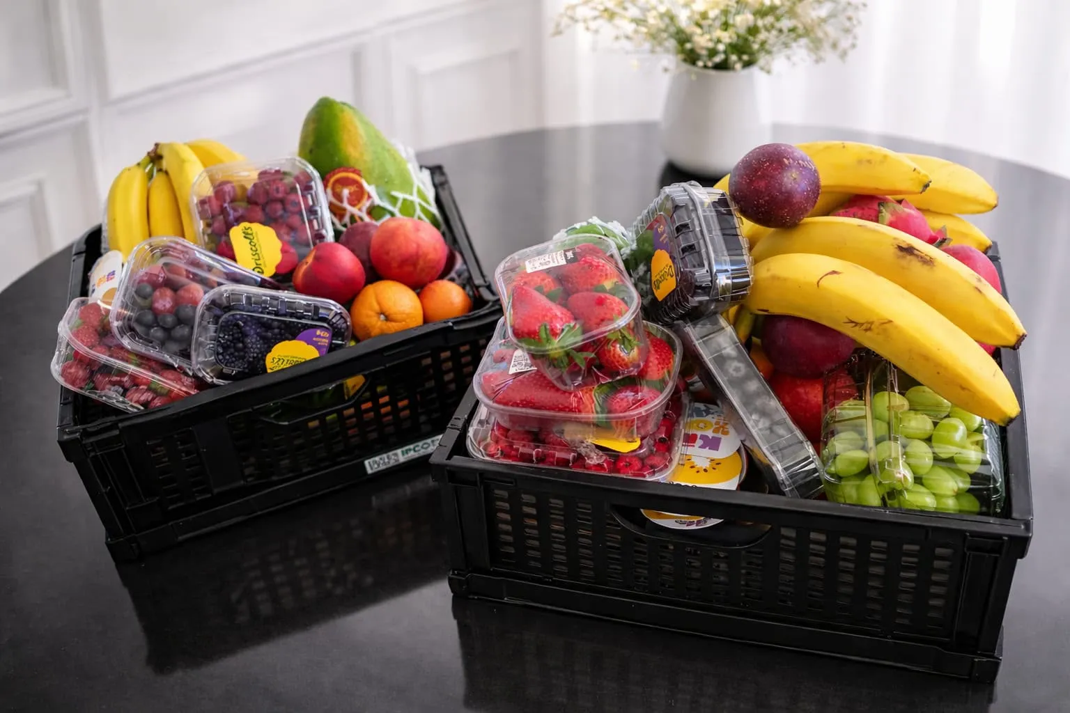Twee zwarte kratten vol bessen, aardbeien, bananen, druiven en papaya